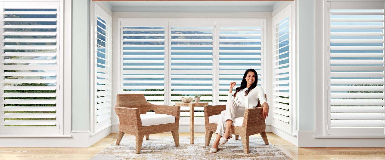 Woman sitting in bay of windows covered with interior shutters.